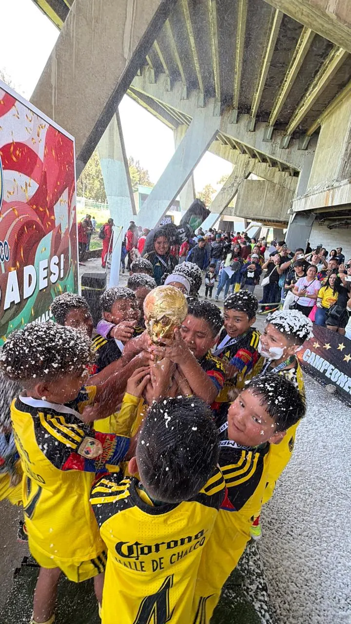 Niños de Nido Águila celebrando con espuma y levantando un trofeo mientras el público los aplaude