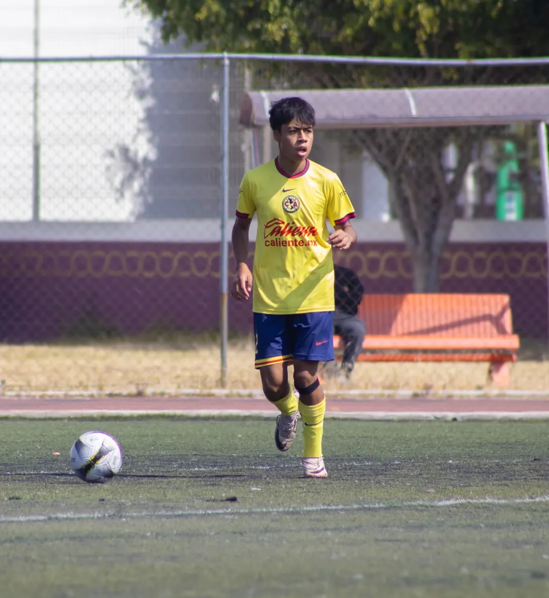Jugador de Nido Águila con camiseta amarilla de pie junto a un balón en la cancha