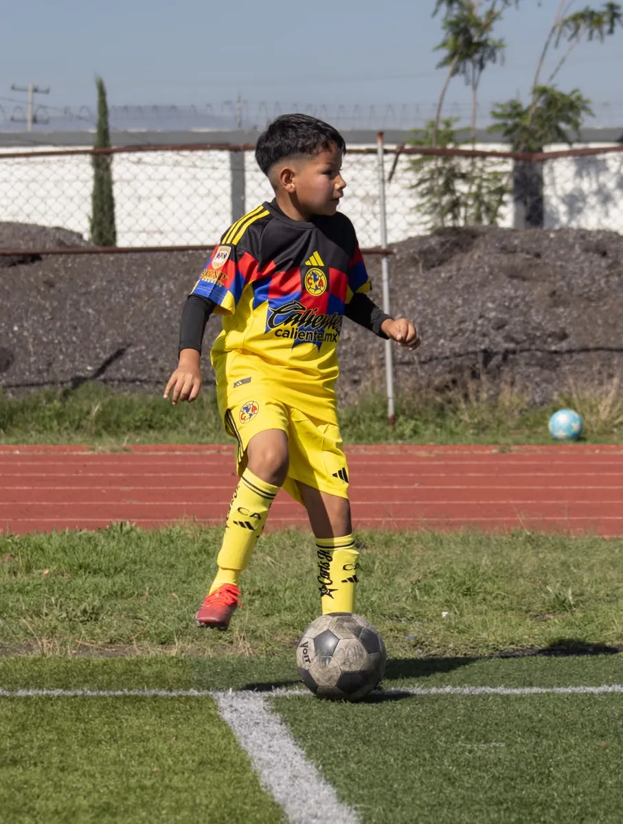 Niño de Nido Águila controlando el balón en la cancha con uniforme amarillo, negro y rojo