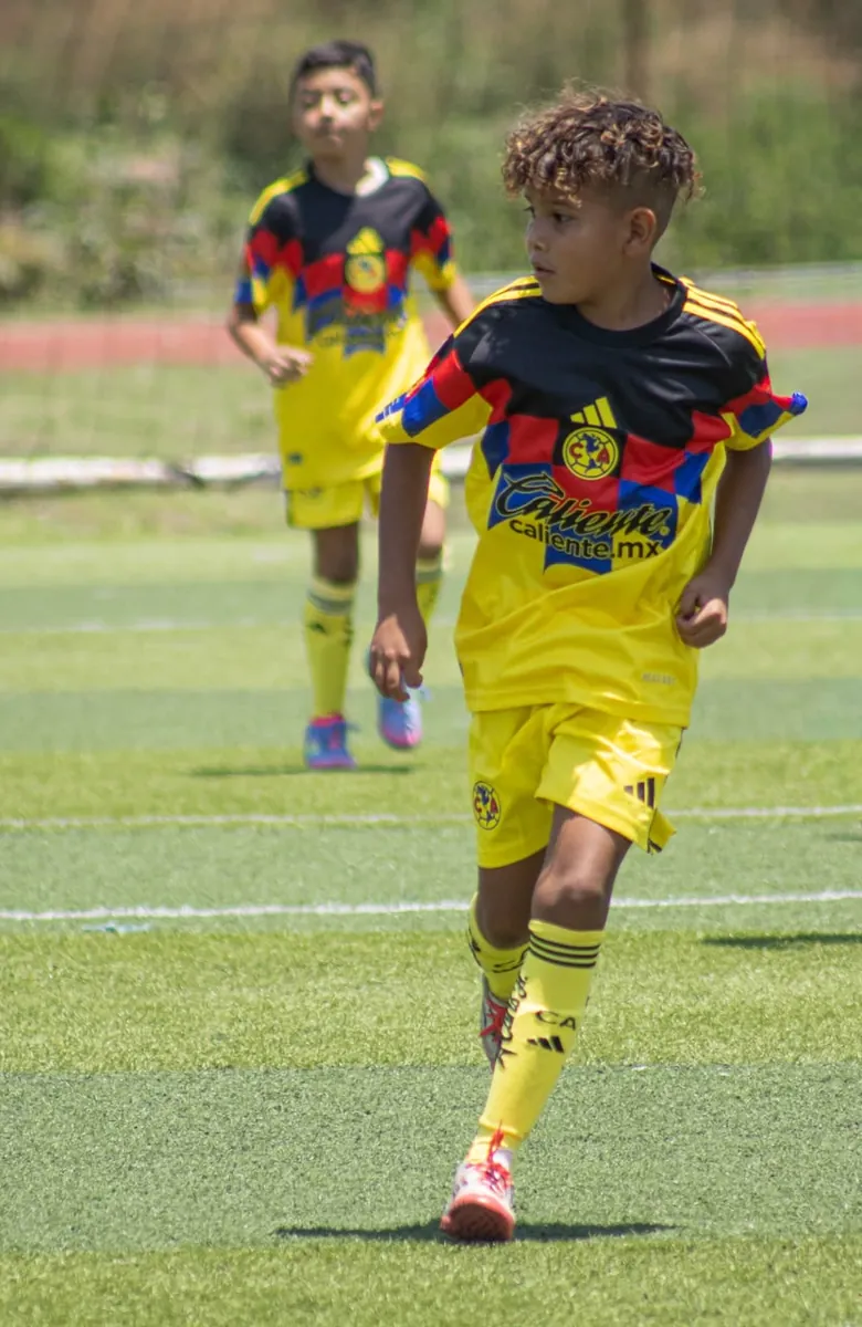 Niño de Nido Águila con uniforme negro, rojo y amarillo corriendo con el balón